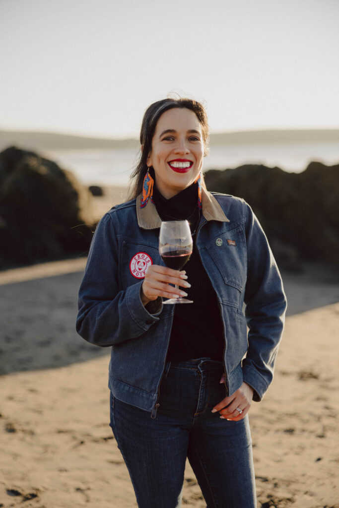 Jessica Jaramillo standing on a beach smiling with a glass of cabernet sauvignon in her hand